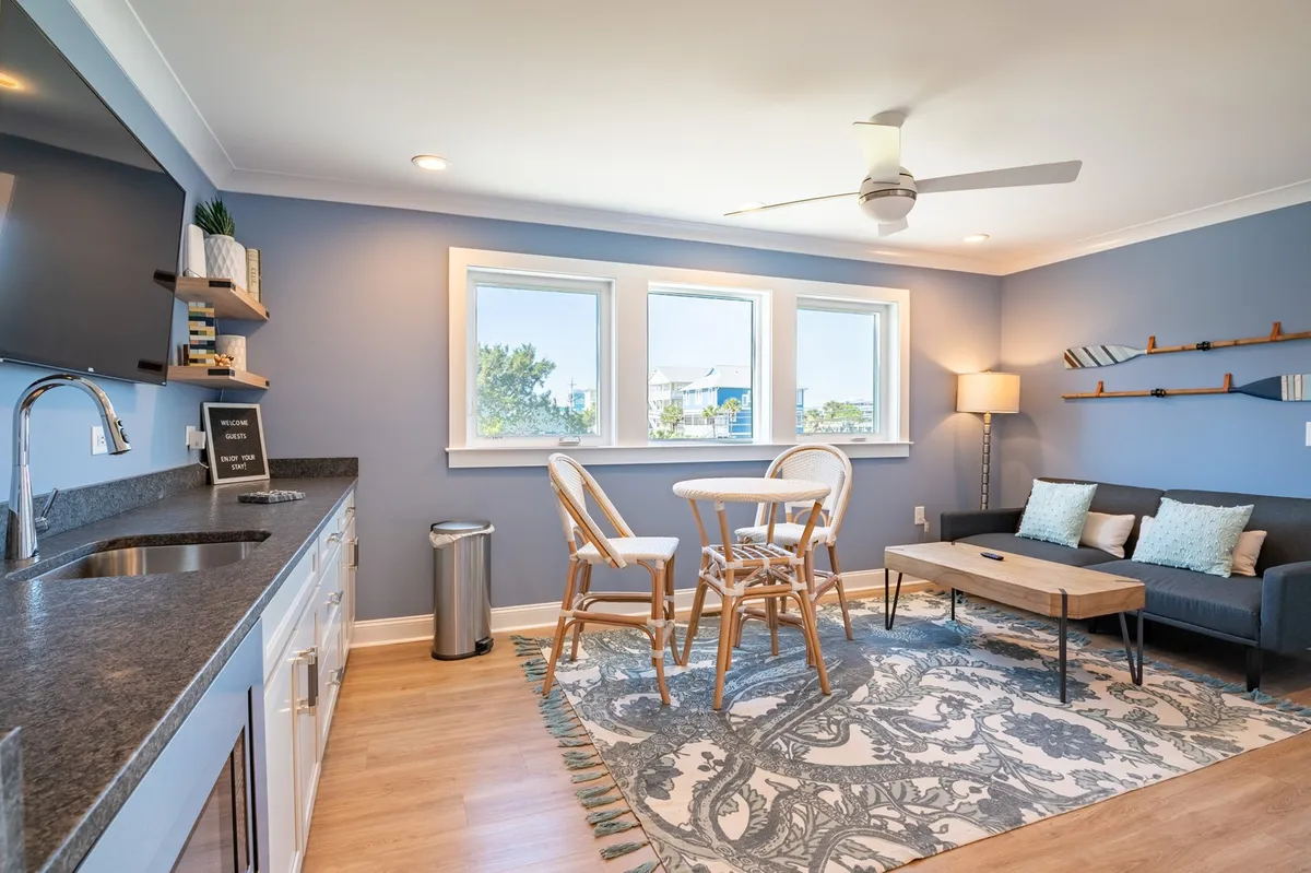 An inviting open area with a kitchen countertop, windows showcasing scenic views, a dining table with chairs, a sofa, and a decorative rug. The room encourages casual dining, reading, and relaxed socializing, characteristic of a boutique-resort ambiance.