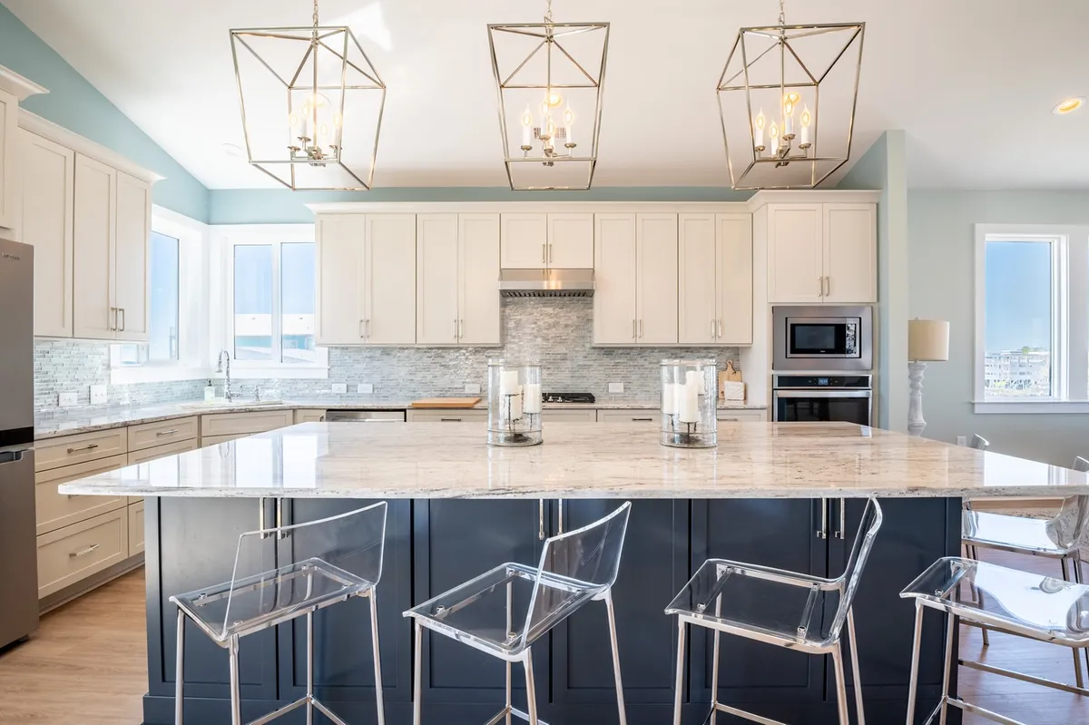 A contemporary, spacious kitchen with a large granite island, stylish pendant lighting, modern cabinetry, and stainless steel appliances dominates this interior scene. The space is designed for group cooking and entertaining, with plenty of seating and an open, inviting feel.