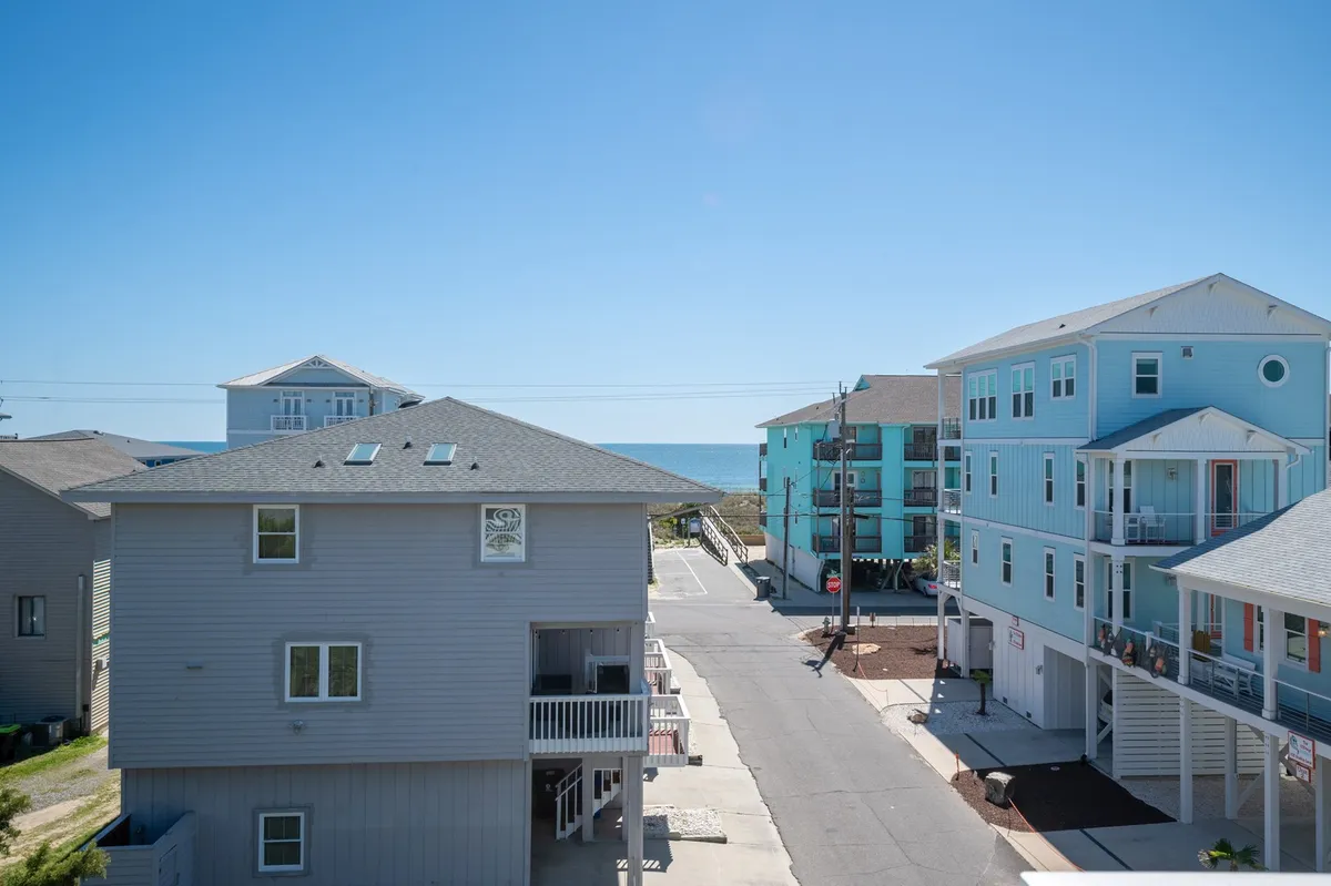 A vibrant exterior shot capturing a stretch of colorful beach houses set against a clear sky, with the sandy beach and ocean just beyond. The scene suggests a lively, inviting shoreline perfect for family walks and outdoor gatherings.
