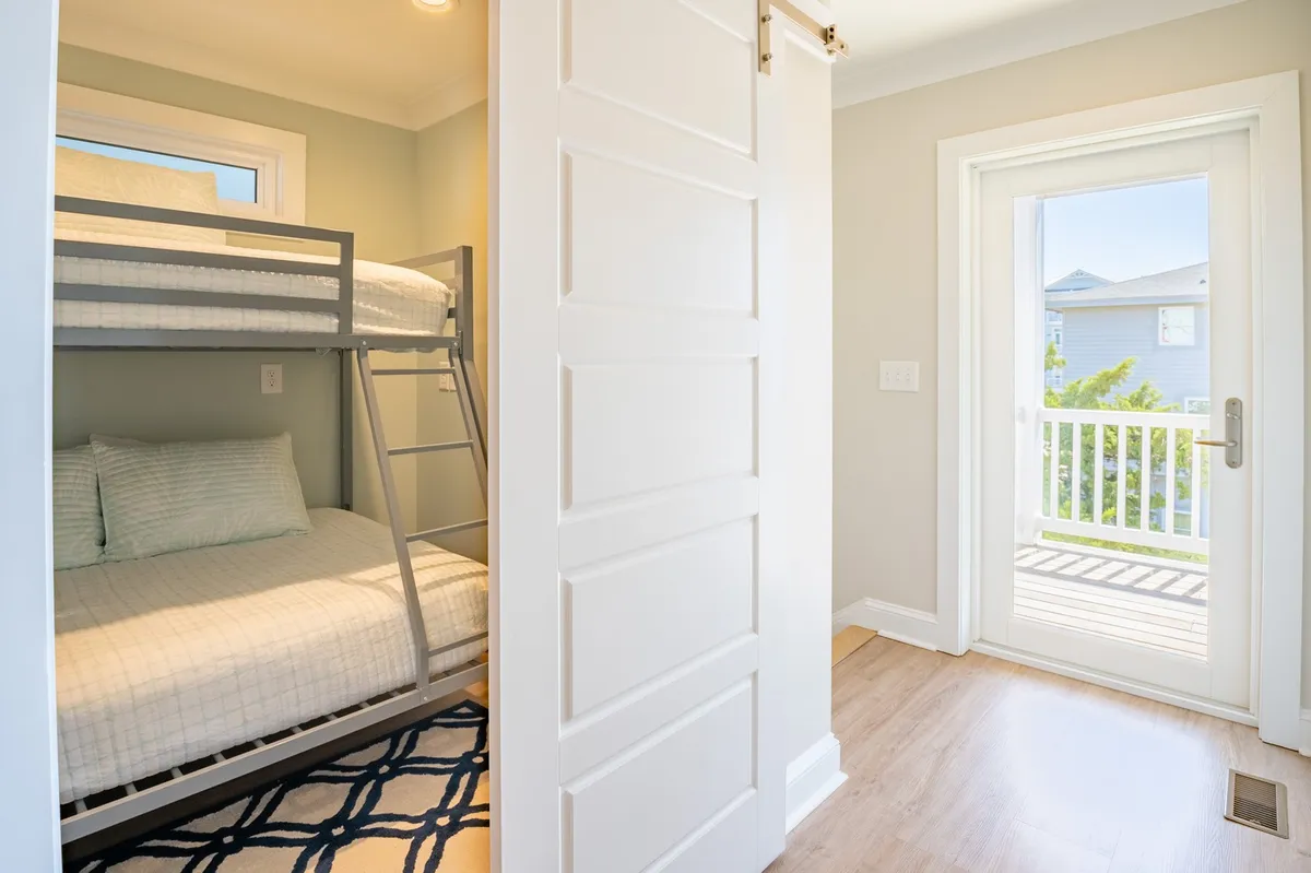 A cozy bunk room with a sturdy bunk bed, door to a private balcony, and a window letting in natural light. The space is inviting and perfect for families or groups.