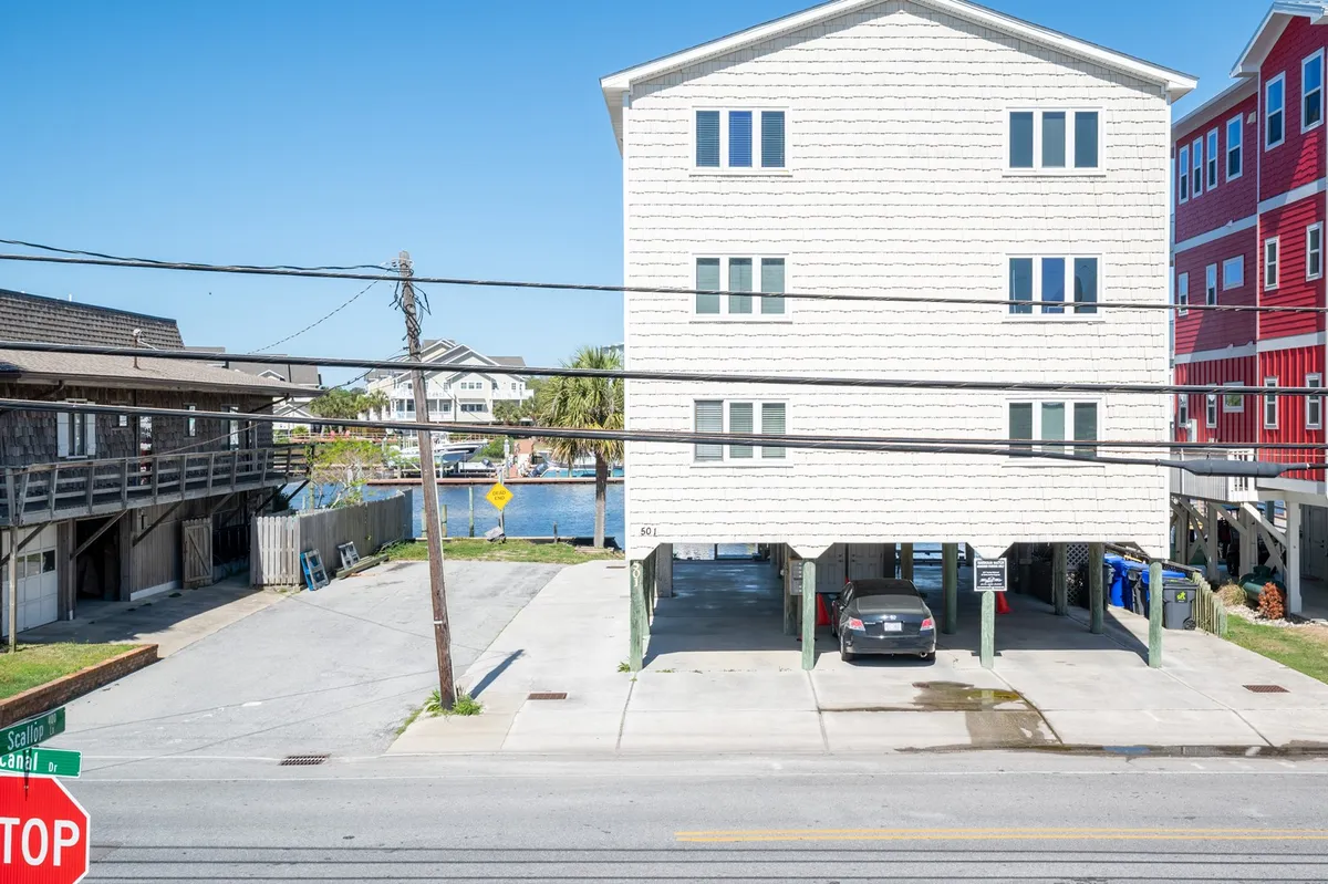The home’s exterior with the water glimmering in the background, visible parking area, and neighborhood setting. The image conveys proximity to the marina and a sense of community within a coastal environment.