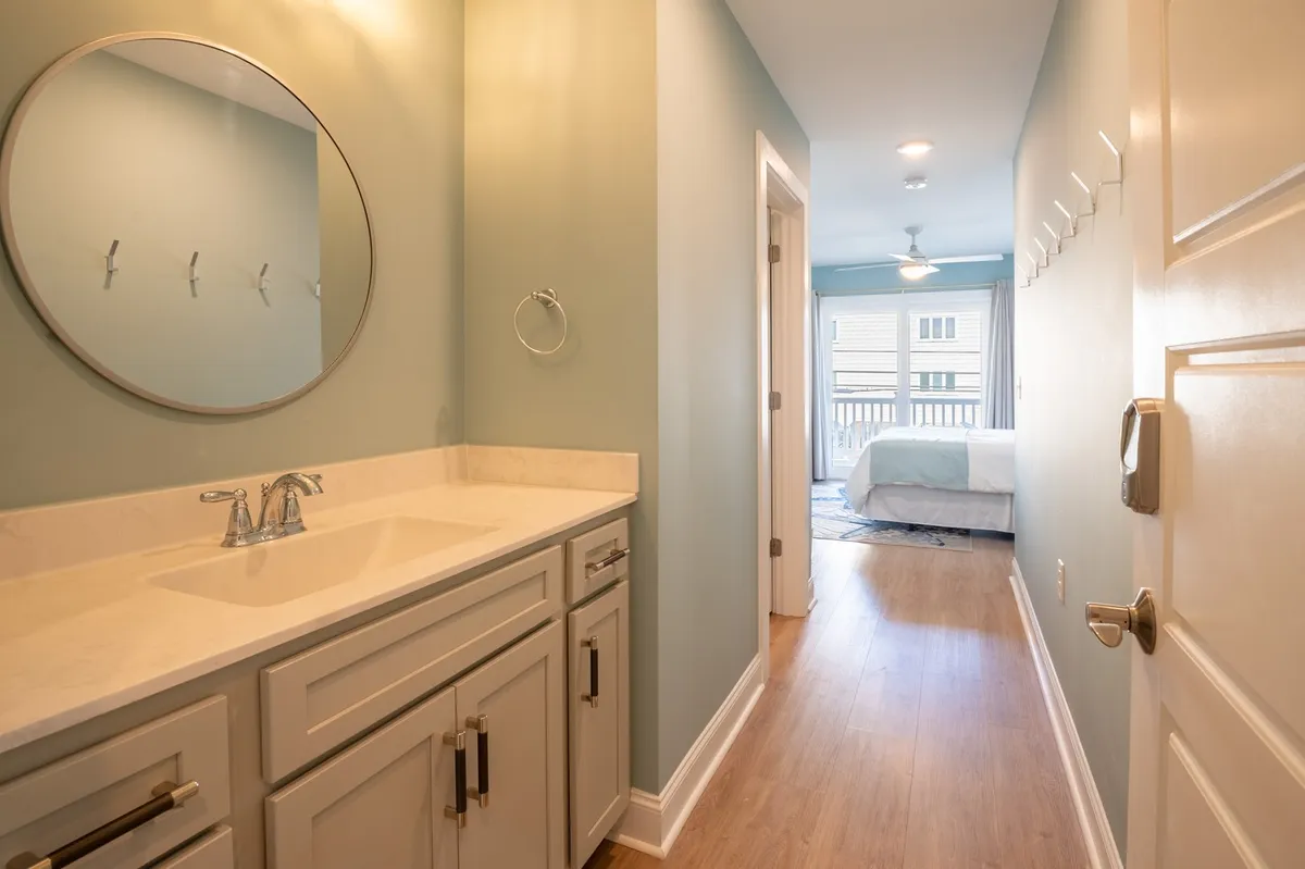 A bathroom vanity with a large mirror and a view into an adjoining bedroom. Soft morning sunlight floods the space, creating a spa-like atmosphere for relaxation and self-care.
