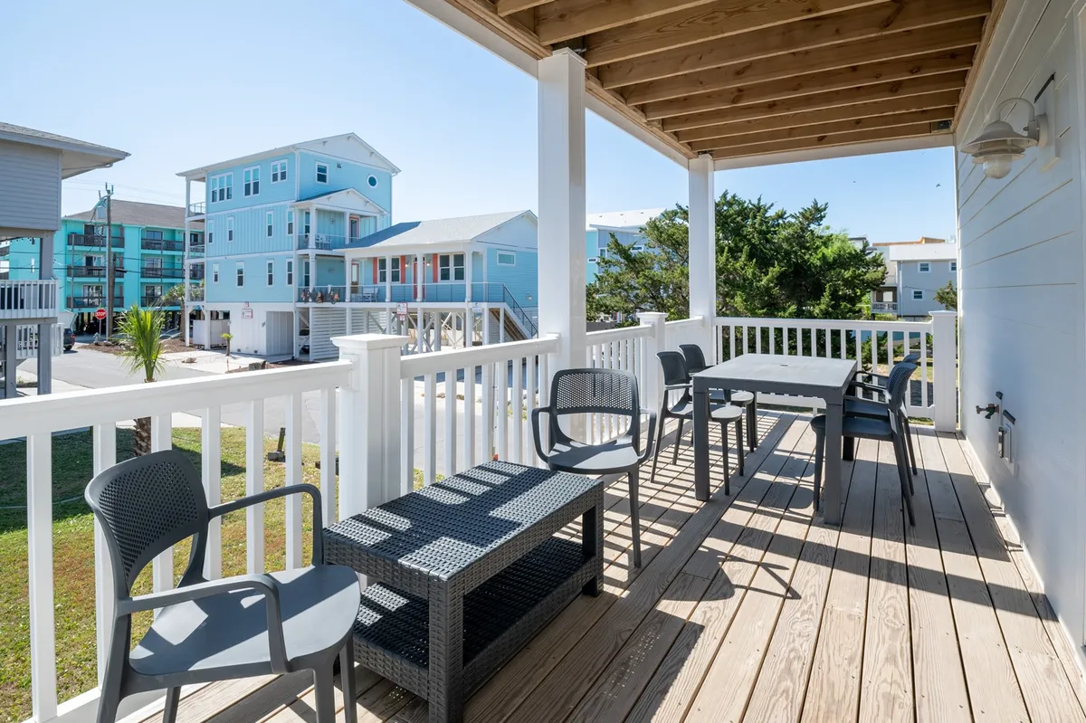 This image captures an inviting outdoor seating area on a deck, with a view of neighboring houses and a wooden railing. The setting is casual, perfect for relaxing with drinks or socializing with friends while enjoying the fresh air and picturesque sunset.